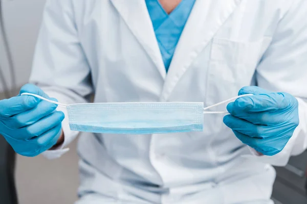 Cropped view of man in blue latex gloves holding medical mask — Stock Photo
