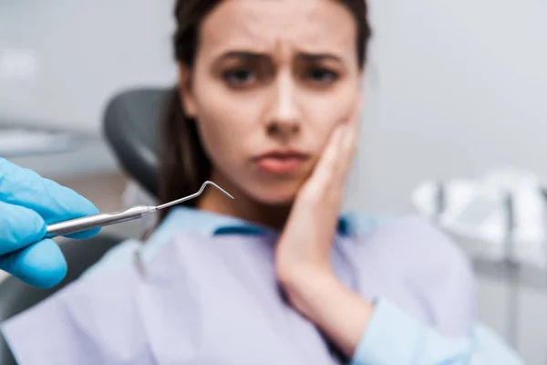 Selektiver Fokus des Zahnarztes im Latexhandschuh, der ein zahnärztliches Instrument in der Nähe einer Frau mit Zahnschmerzen hält — Stockfoto