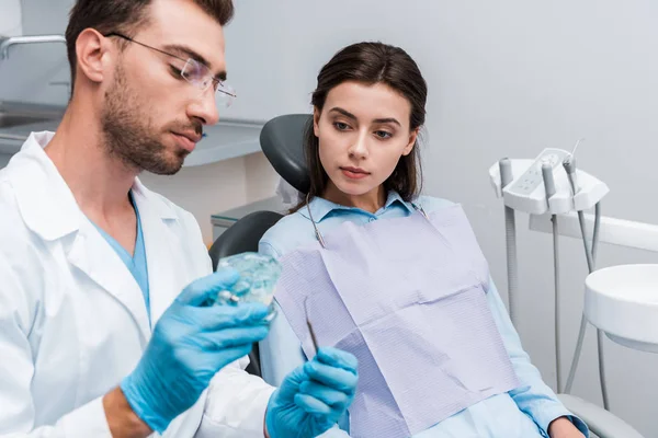 Selective focus of attractive woman looking at retainer in hands of handsome dentist in glasses — Stock Photo