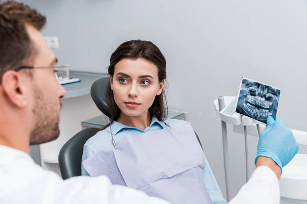 Selective focus of attractive woman looking at dentist with x-ray — Stock Photo