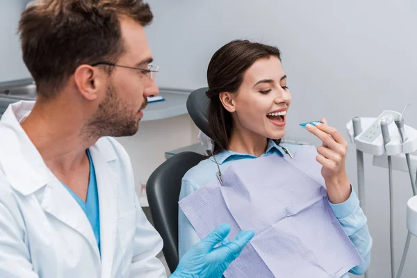 Selective focus of cheerful woman looking at retainer near handsome dentist in glasses — Stock Photo