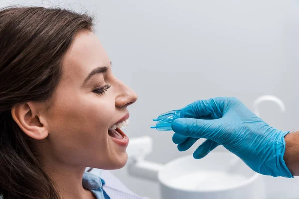 Обрезанный вид стоматолога в латексной перчатке с фиксатором рядом с веселой девушкой — стоковое фото