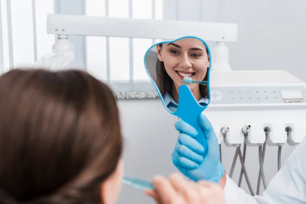 Foyer sélectif de fille brossant les dents et regardant miroir près du dentiste — Photo de stock