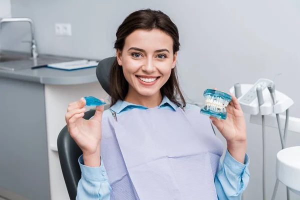 Alegre joven mujer sosteniendo dientes modelo y retenedor en las manos - foto de stock