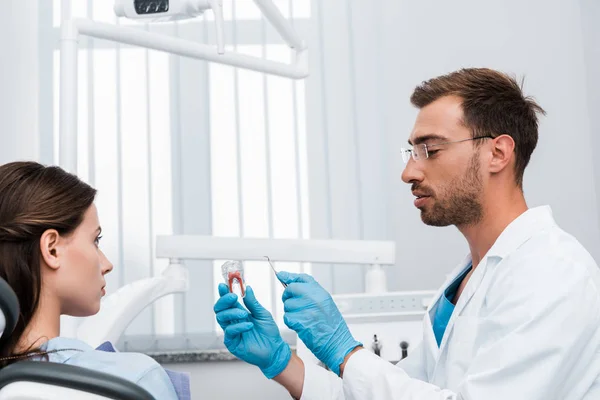 Messa a fuoco selettiva del dentista in occhiali che tengono strumento dentale e modello di dente vicino alla ragazza — Stock Photo