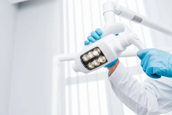 Cropped view of dentist in latex gloves touching medical lamp — Stock Photo