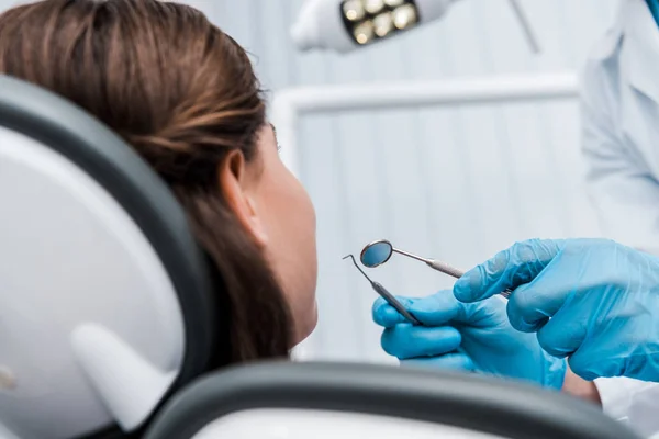 Cropped view of dentist in blue latex gloves holding dental instruments near woman — Stock Photo