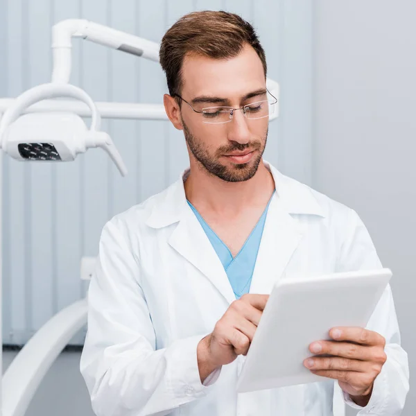 Bel homme barbu en manteau blanc et lunettes à l'aide d'une tablette numérique — Photo de stock