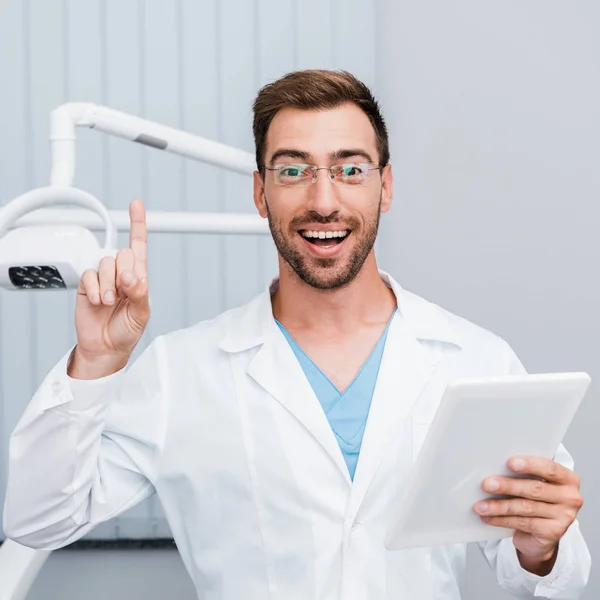 Glücklicher bärtiger Mann in weißem Mantel und Brille gestikuliert in der Hand eines digitalen Tablets — Stockfoto