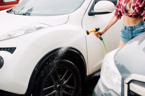 Vista ritagliata della ragazza che lava auto bianca mentre tiene in mano la rondella di pressione — Foto stock