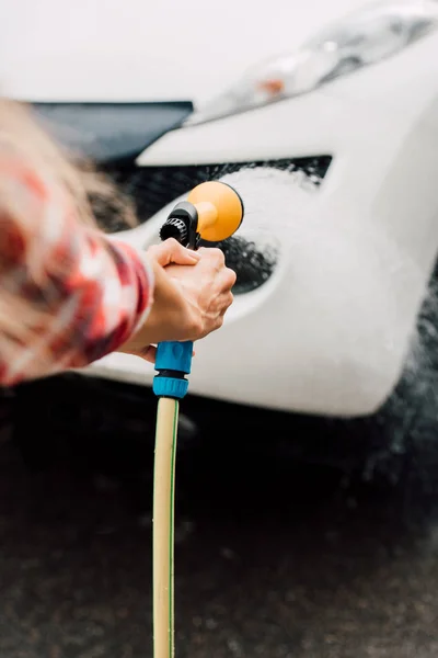 Vista ritagliata della donna che lava l'automobile mentre tiene la rondella di pressione — Foto stock