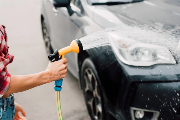 Vue recadrée de femme lavage voiture noire tout en tenant laveuse sous pression — Photo de stock