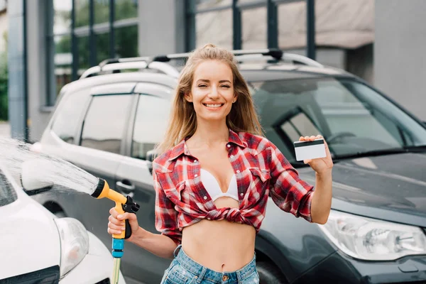 Весела дівчина тримає мийку під тиском і кредитну картку біля автомобілів — стокове фото