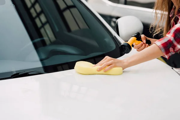 Vista recortada de la joven mujer sosteniendo esponja mientras lava el coche - foto de stock