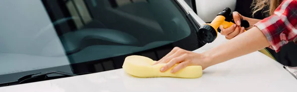 Tiro panorámico de mujer joven sosteniendo esponja mientras lava el coche - foto de stock