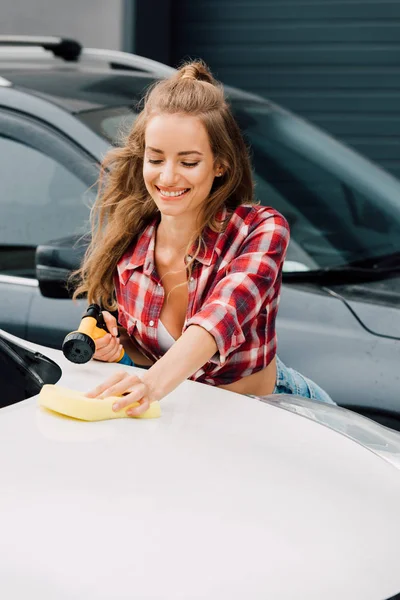 Happy girl holding pressure washer and sponge while washing car — Stock Photo