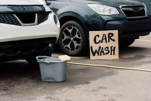 Voitures blanches et noires près seau et carton avec lettres de lavage de voiture — Photo de stock