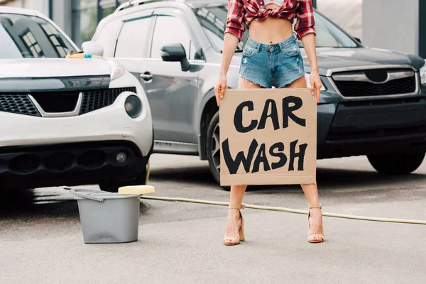 Обрезанный вид девушки, стоящей и держащей картонный плакат с автомойкой буквы возле автомобилей — стоковое фото