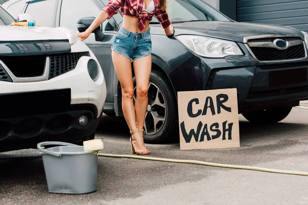 Обрізаний вид на дівчину, що стоїть поруч з машинами і плакат з листами автомийки — стокове фото