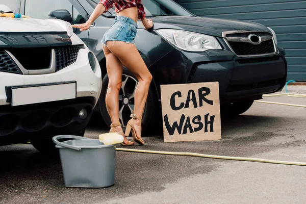 Cropped view of girl standing near cars and placard with car wash letters — Stock Photo