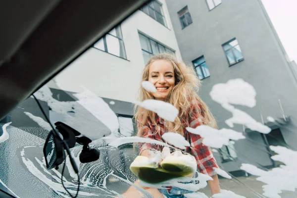 Vista basso angolo di felice ragazza lavaggio auto con spugna — Foto stock