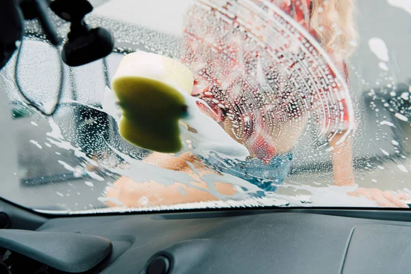 Selective focus of young woman washing windshield of car with sponge — Stock Photo