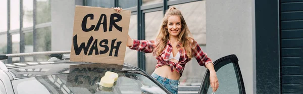 Colpo panoramico di felice ragazza che tiene cartello con auto lavaggio lettering vicino auto — Foto stock