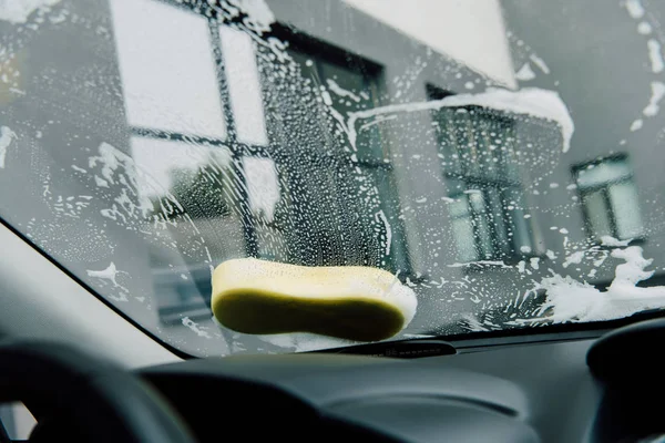 Éponge jaune humide sur le pare-brise de la voiture près du bâtiment — Photo de stock