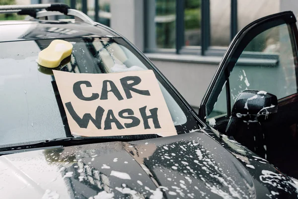 Cartone con scritta autolavaggio su automobile bagnata con schiuma — Foto stock