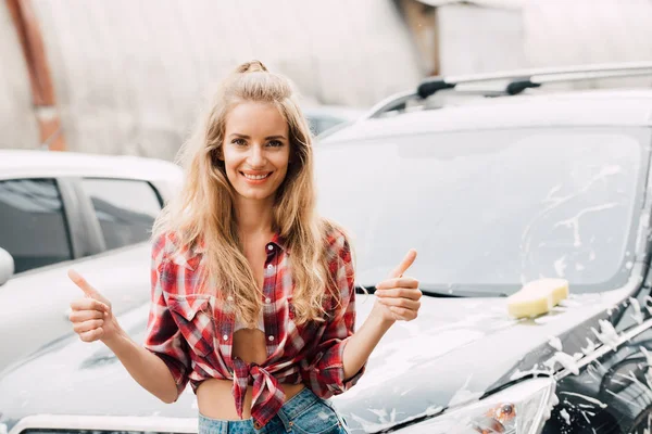 Menina feliz mostrando polegares para cima e sorrindo perto de carros — Fotografia de Stock