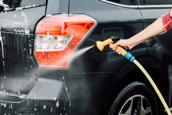 Ausgeschnittene Ansicht einer Frau, die schwarzes Auto wäscht und Hochdruckreiniger hält — Stockfoto