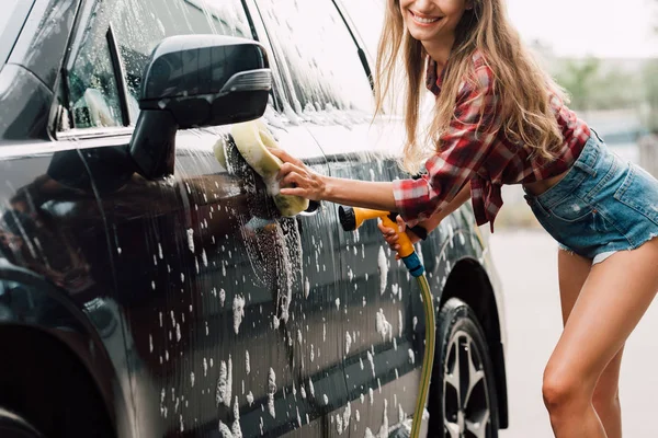 Vista ritagliata della ragazza positiva lavaggio auto bagnata in schiuma — Foto stock