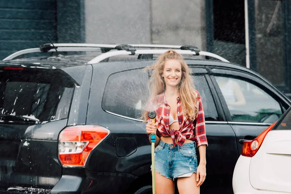 Щаслива жінка тримає портативну пральну машину і стоїть біля автомобілів — стокове фото