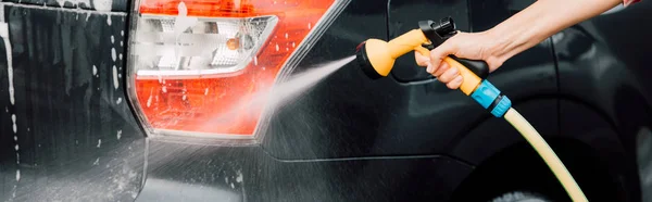 Panoramic shot of girl woman washing black car and holding pressure washer — Stock Photo