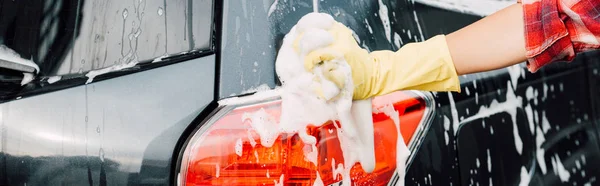 Panoramic shot of girl in latex glove near wet car in foam — Stock Photo