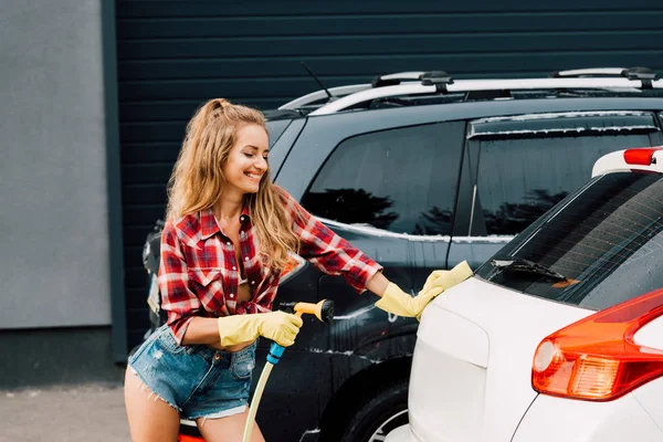 Sonriente mujer en guantes de látex sosteniendo la presión de la lavadora - foto de stock