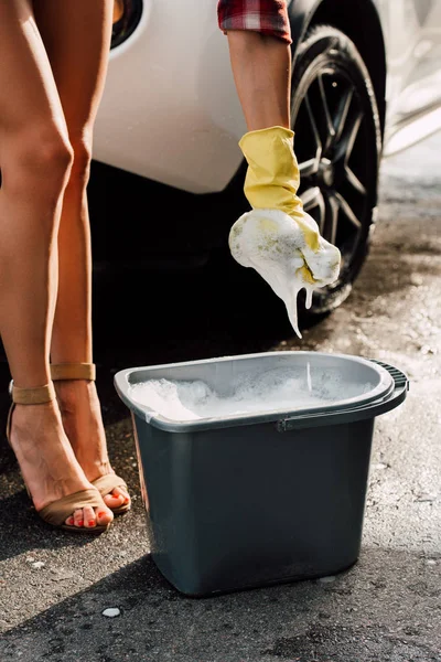 Vista ritagliata della ragazza che tiene la spugna in schiuma vicino al secchio con acqua — Foto stock