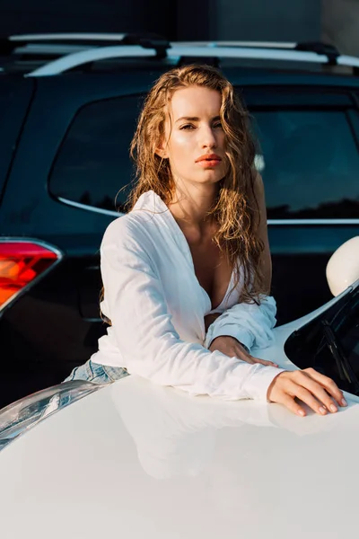 Сексуальная молодая женщина смотрит в камеру рядом с белой машиной — стоковое фото
