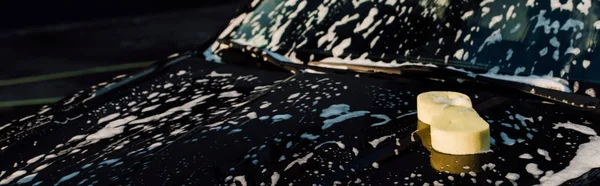 Панорамна жовта губка на мокрій і розкішній чорний автомобіль в автомийці — стокове фото