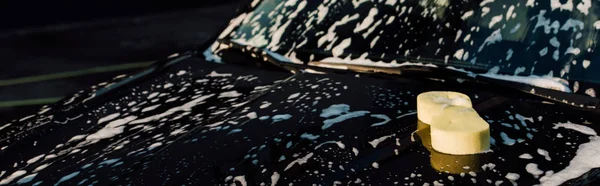 Panoramic of yellow sponge on wet and luxury black automobile in car wash — Stock Photo