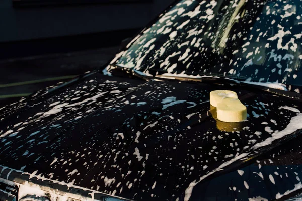 Yellow sponge on wet and luxury black automobile in car wash — Stock Photo