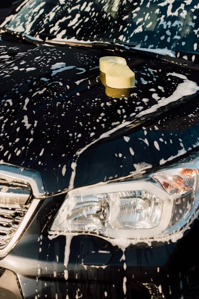 Esponja amarela no carro preto molhado e luxuoso na espuma — Fotografia de Stock