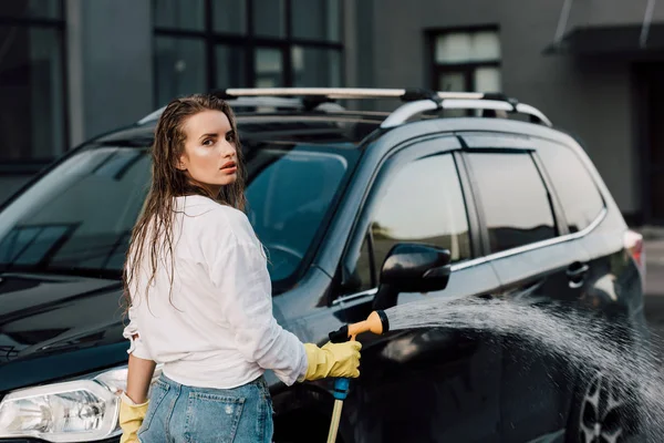 Nasses Mädchen hält Hochdruckreiniger in der Nähe von schwarzem Auto — Stockfoto