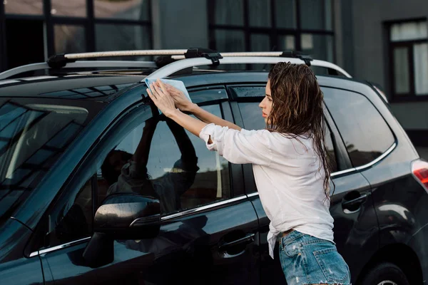 Attraktives und nasses Mädchen wäscht schwarzes Luxusauto mit blauem Tuch — Stockfoto