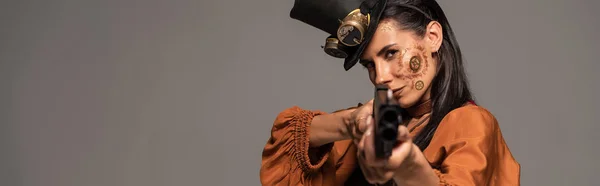 Panoramic shot of focused steampunk woman aiming with pistol at camera isolated on grey — Stock Photo