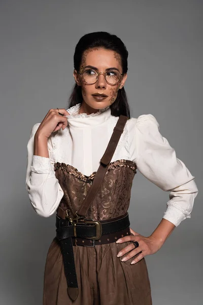 Vista frontal de una mujer steampunk pensativa con maquillaje mirando hacia otro lado aislado en gris - foto de stock