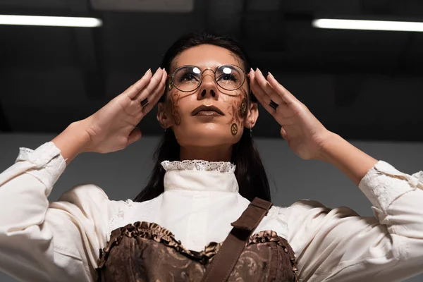 Baixo ângulo vista de steampunk mulher tocando óculos e olhando para cima — Fotografia de Stock