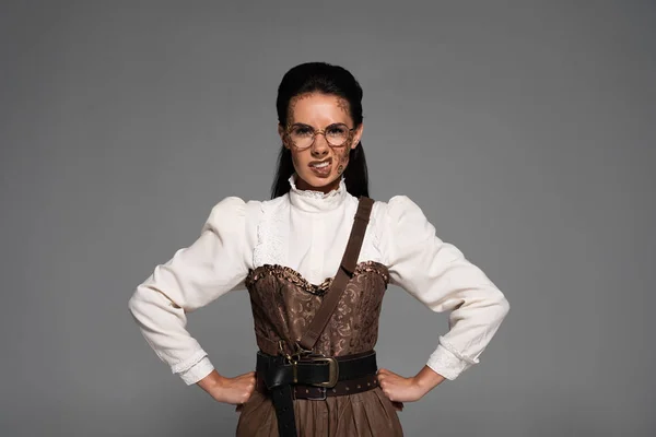 Vista frontal de mujer steampunk enojada en gafas de pie con las manos en las caderas aisladas en gris - foto de stock