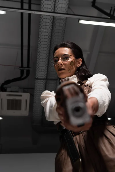 Избирательный фокус уверенной стимпанк-женщины, нацеленной с пистолетом на камеру — стоковое фото