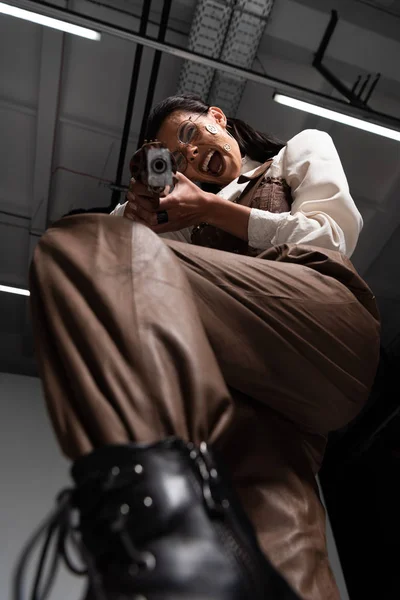 Low angle view of screaming steampunk woman aiming with pistol at camera — Stock Photo